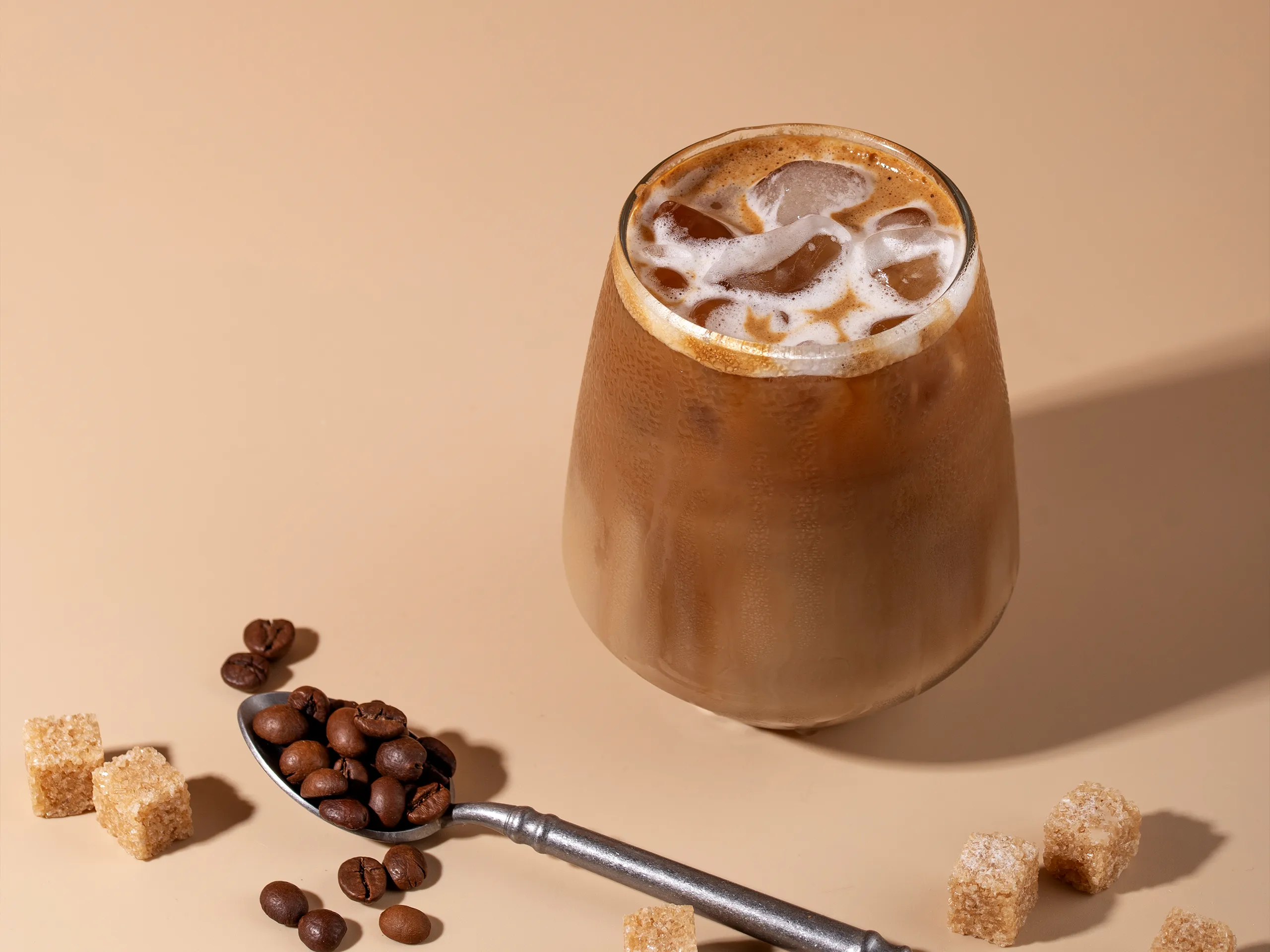 Iced Latte im Glas mit Eisw&uuml;rfeln, Kaffeebohnen und braunem Zucker