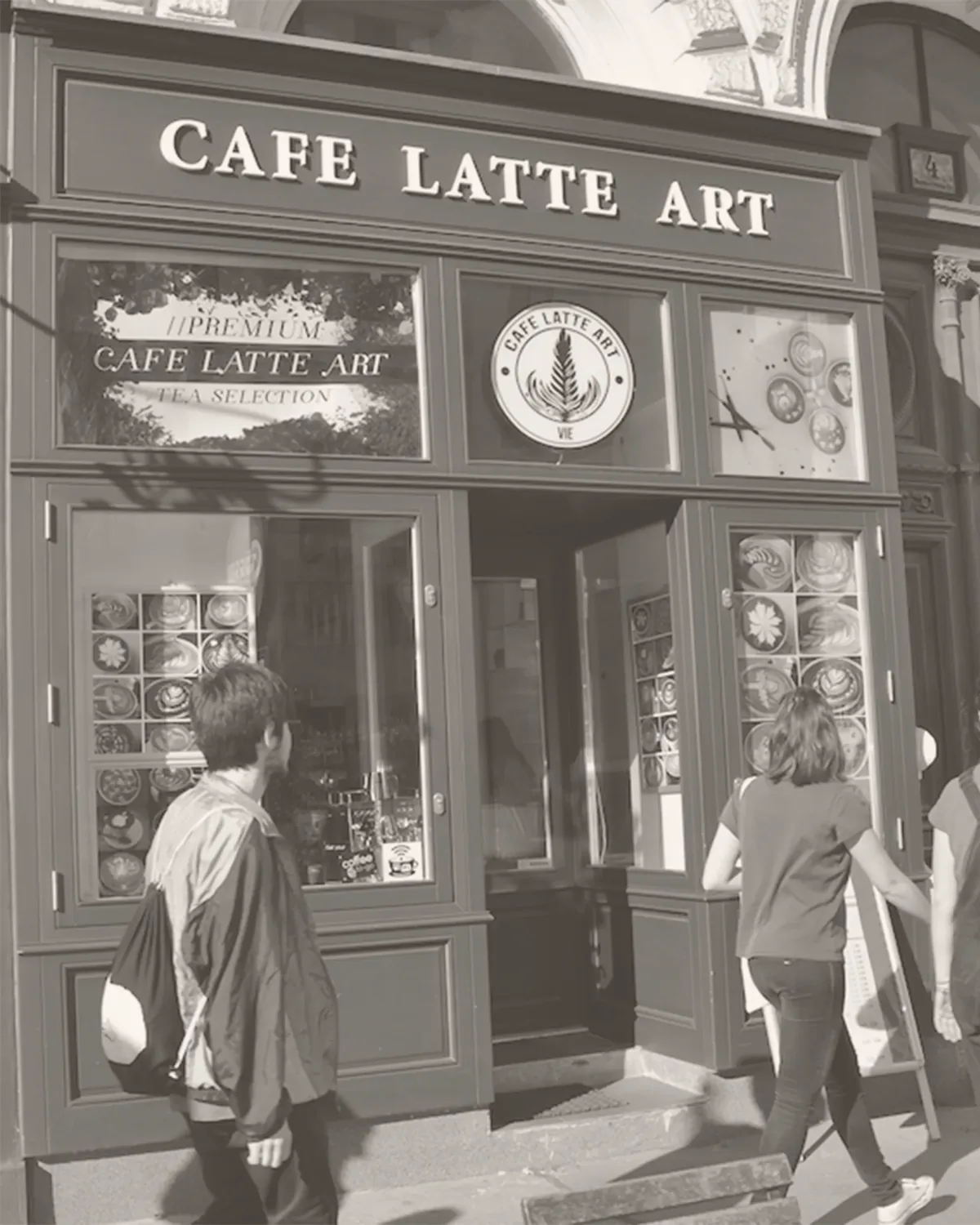 Die Au&szlig;enansicht von Cafe Latte Art in der Universit&auml;tsstra&szlig;e 4 in Wien, Schwarzwei&szlig;aufnahme mit Passanten vor der Auslage