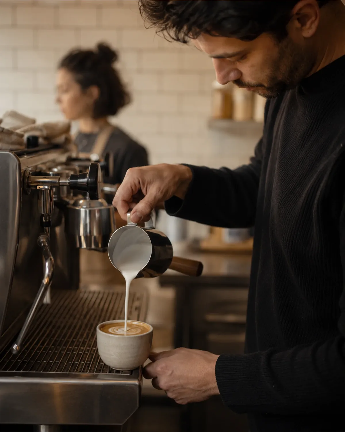 Barista gie&szlig;t Milch aus der Kanne in eine Tasse an der Siebtr&auml;germaschine